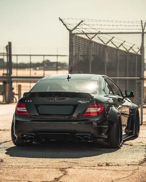 Black Mercedes C63 by a chain-link fence at golden hour